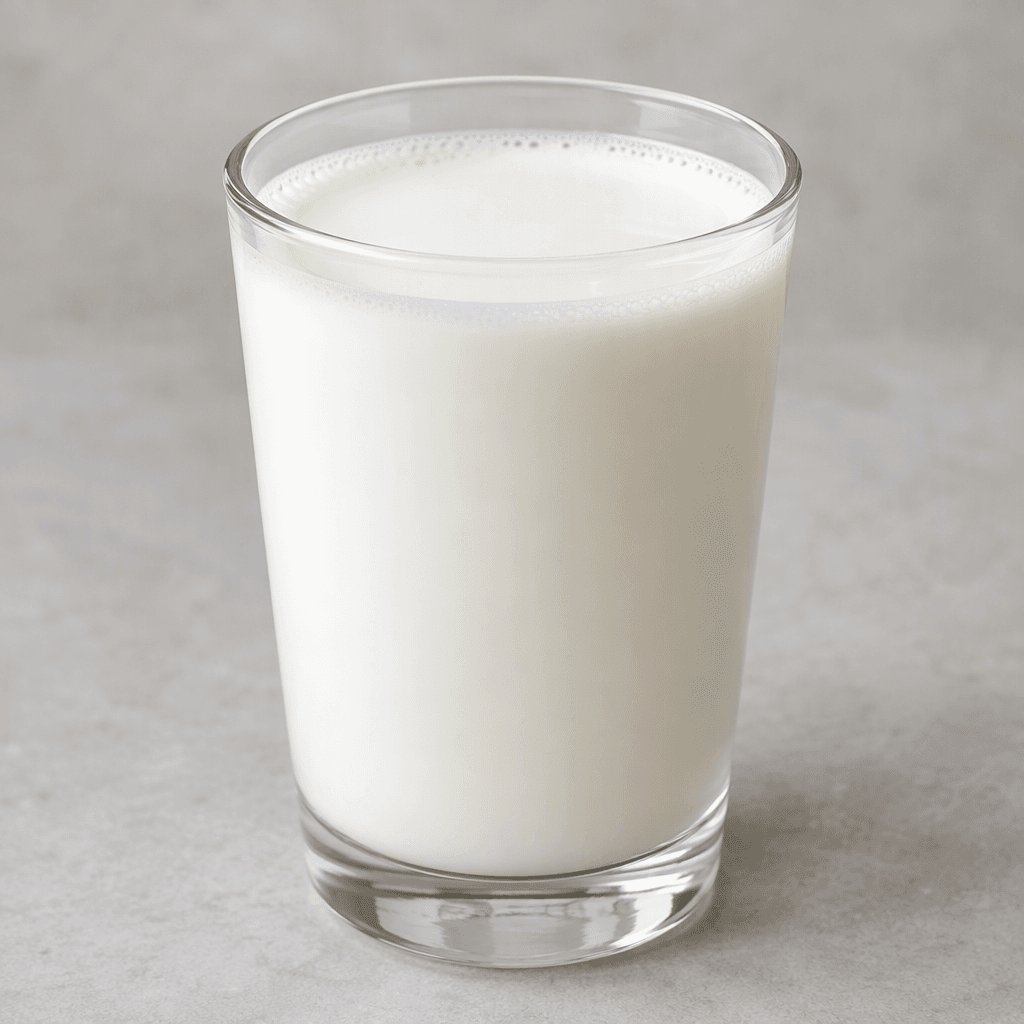 A clear glass filled with smooth, opaque white liquid, with a clean, slightly glossy surface and a thin pale ring of foam along the rim.