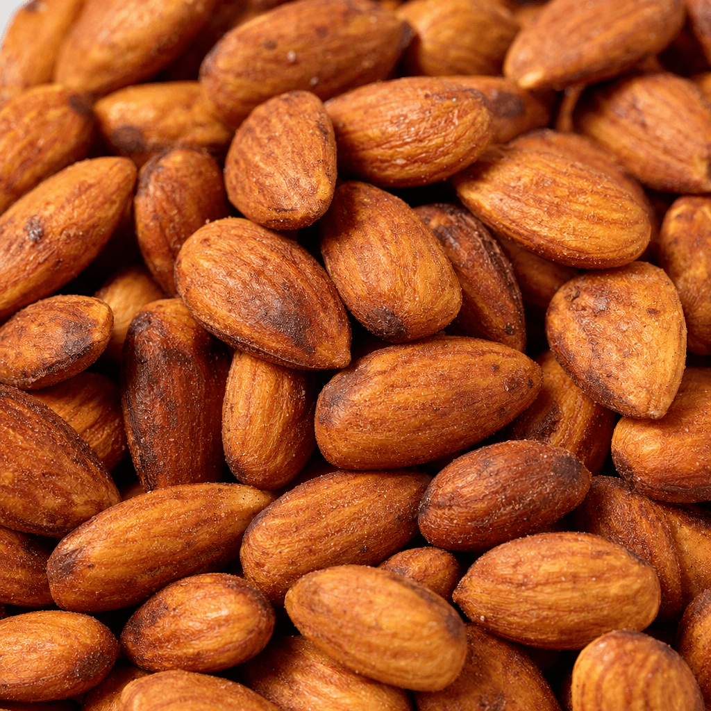 Whole roasted almonds with elongated oval shapes, pointed tips, and warm golden-brown skins lightly mottled with darker toasted spots, piled loosely together.