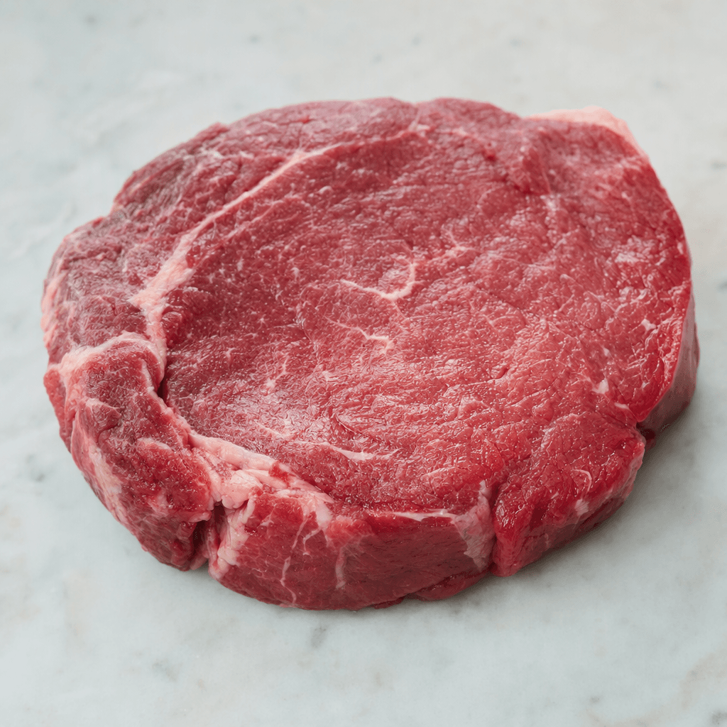 A thick, irregularly oval cut of raw beef with a deep red surface, fine pale streaks of fat and a slight moist sheen.