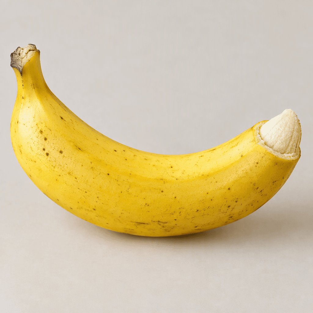 A large, elongated banana with a gently curved shape, thick bright-yellow peel, faint brown speckles, and a pale cream flesh tip visible where one end is peeled back.