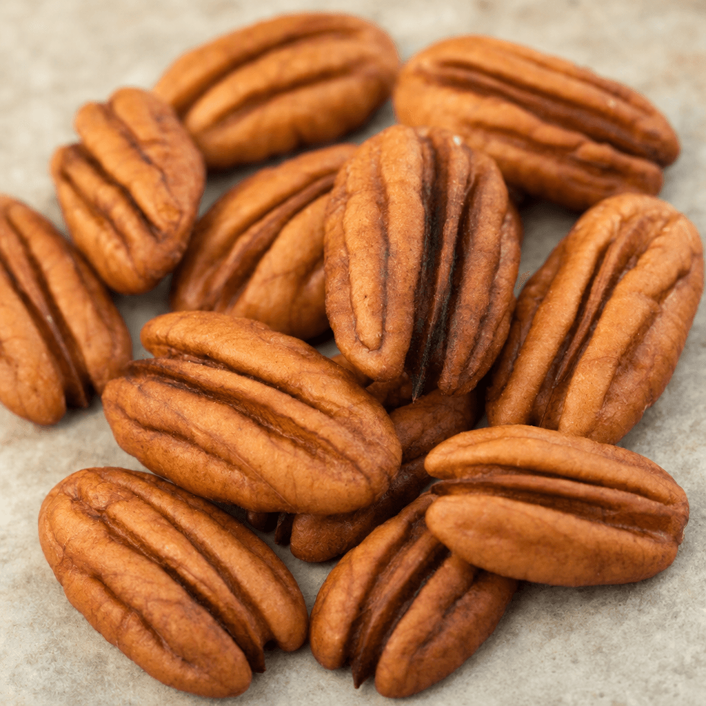Several pecans lie loosely scattered, their elongated oval shells ridged and pointed at both ends, with warm reddish-brown surfaces and fine grooves.