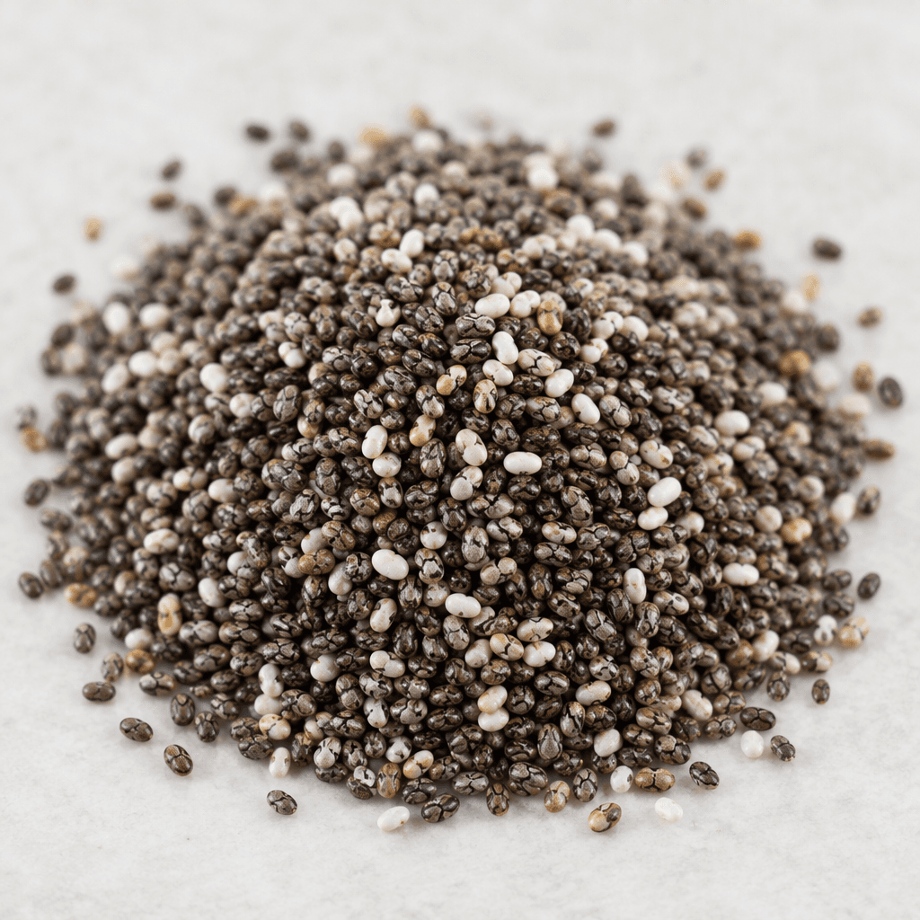 Tiny, dry oval chia seeds with mottled black, white, gray, and brown coloring form a loose pile.