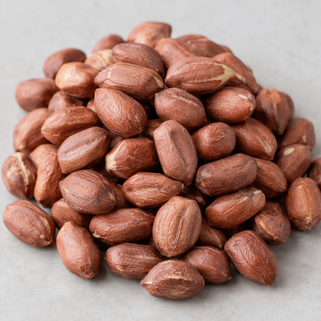 A loose pile of raw peanut kernels with pale cream, knobbly oval bodies and thin reddish-brown skins, showing shallow grooves and slightly uneven surfaces.