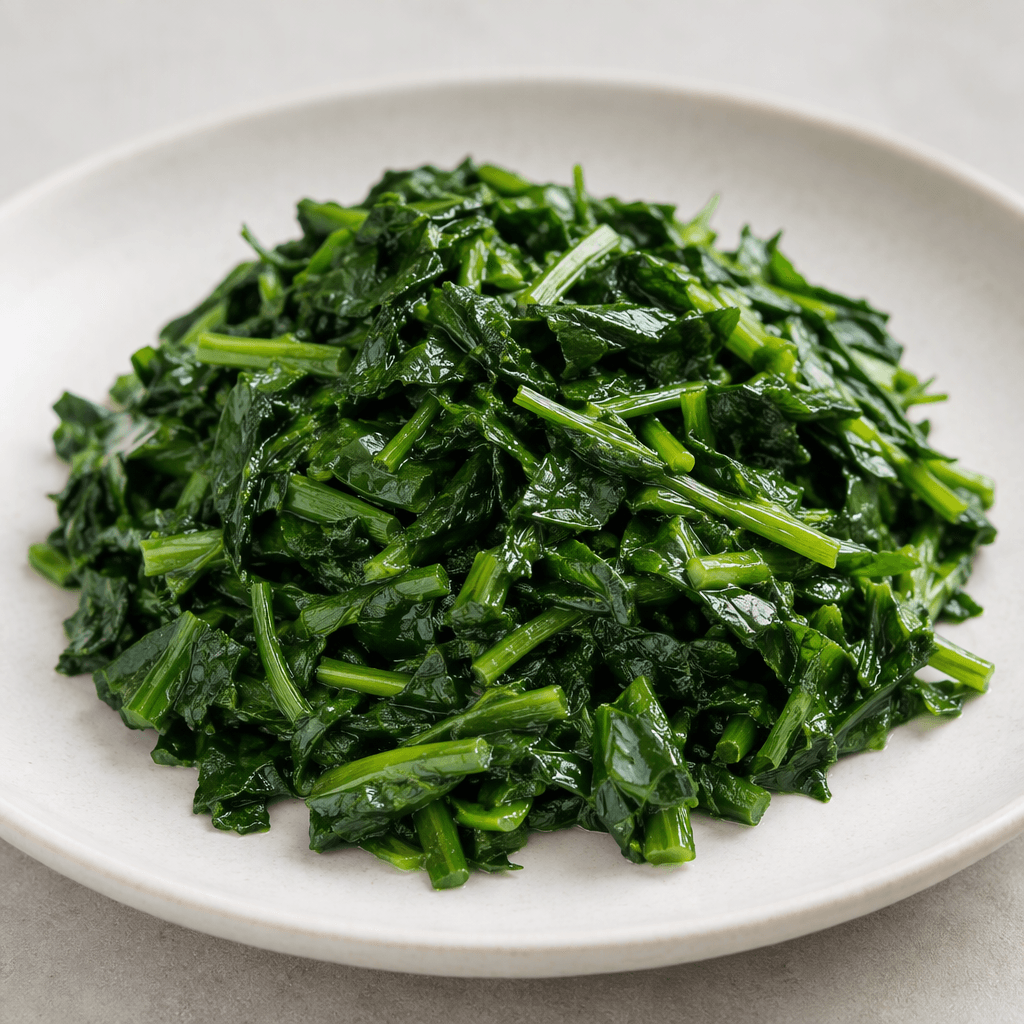 A heap of finely chopped, wilted wild garlic leaves and slender stems, deep green with a slight sheen, served on a plain plate.