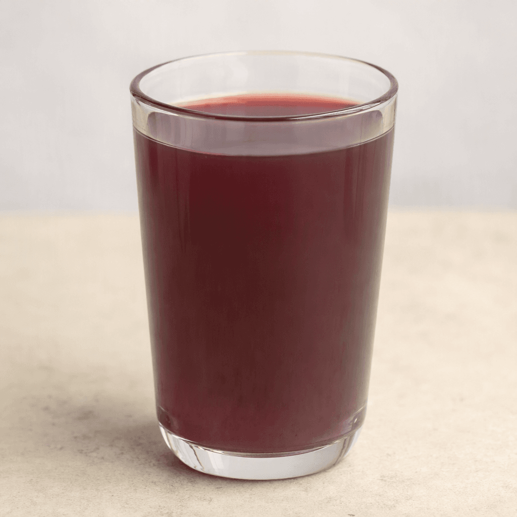 Dark reddish-purple grape juice fills a clear glass, with a smooth surface and a slightly cloudy, translucent appearance.