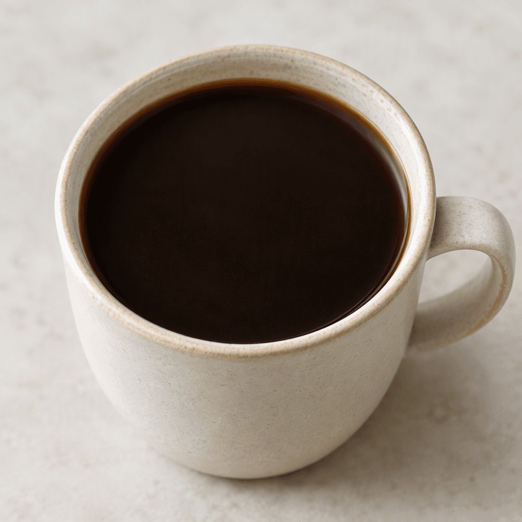 A cup of deep brown, nearly black chicory coffee with a smooth, opaque surface, served hot in a simple mug.