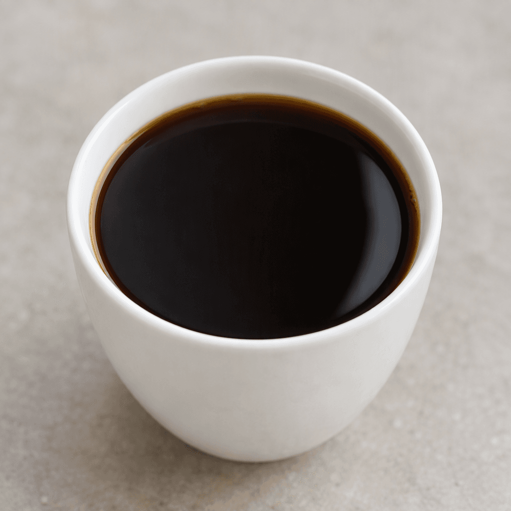 A clear, nearly black-brown liquid with a smooth reflective surface, served unsweetened in a small plain cup, with no visible milk, cream, sugar, or garnish.