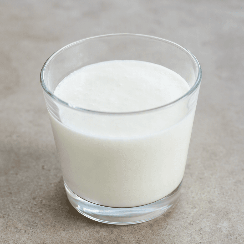 A small clear glass filled with opaque white kefir, its smooth, slightly thick liquid surface level and unadorned.