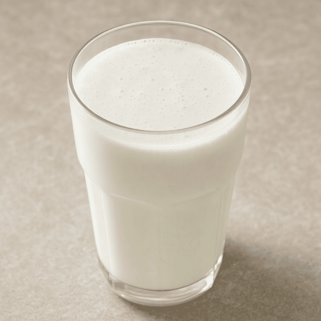 A glass of opaque, milky-white kefir with a smooth, slightly thick consistency and a few tiny bubbles on its surface.