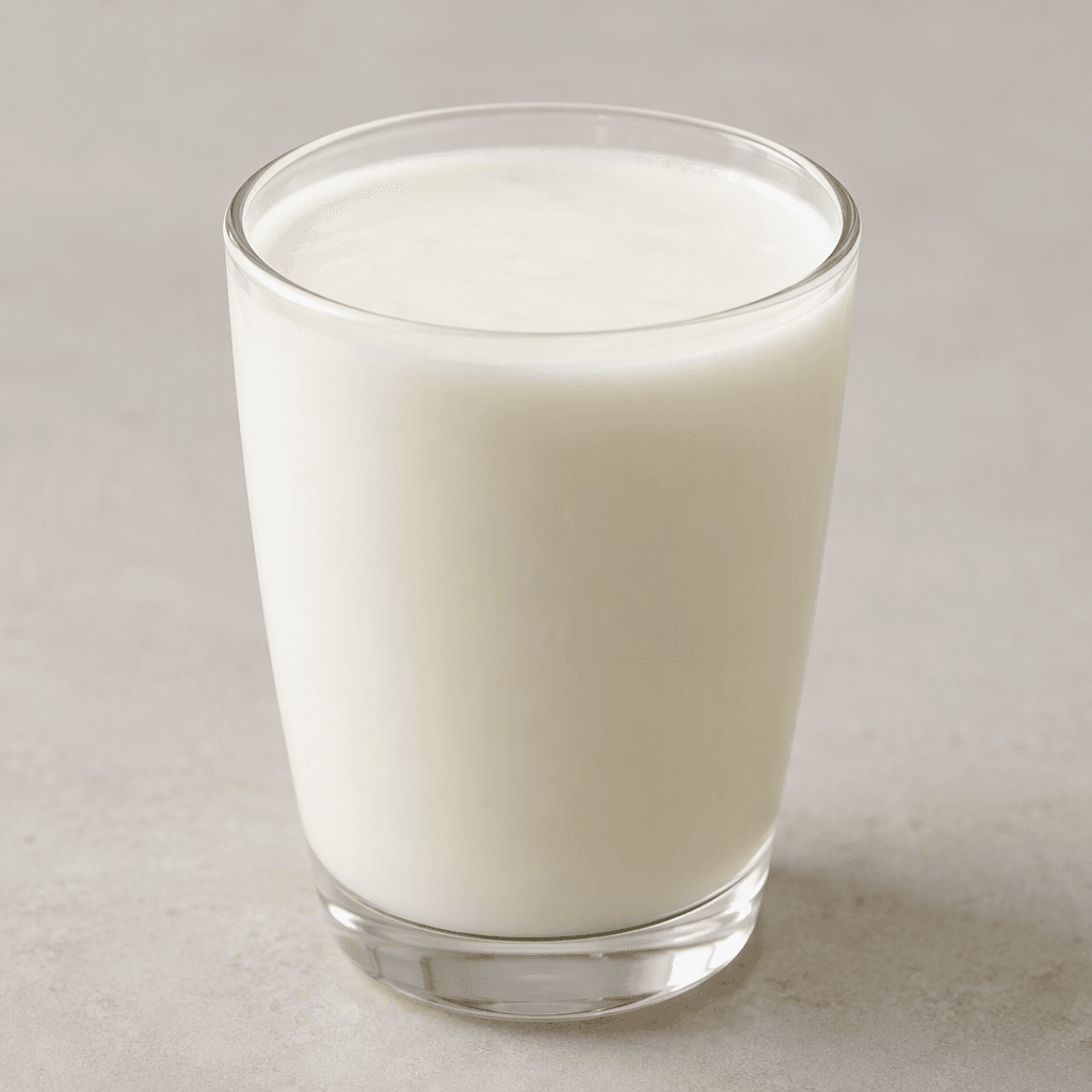 A pale ivory-white, smooth, slightly thick fermented milk drink sits in a clear glass, with a uniform creamy surface.