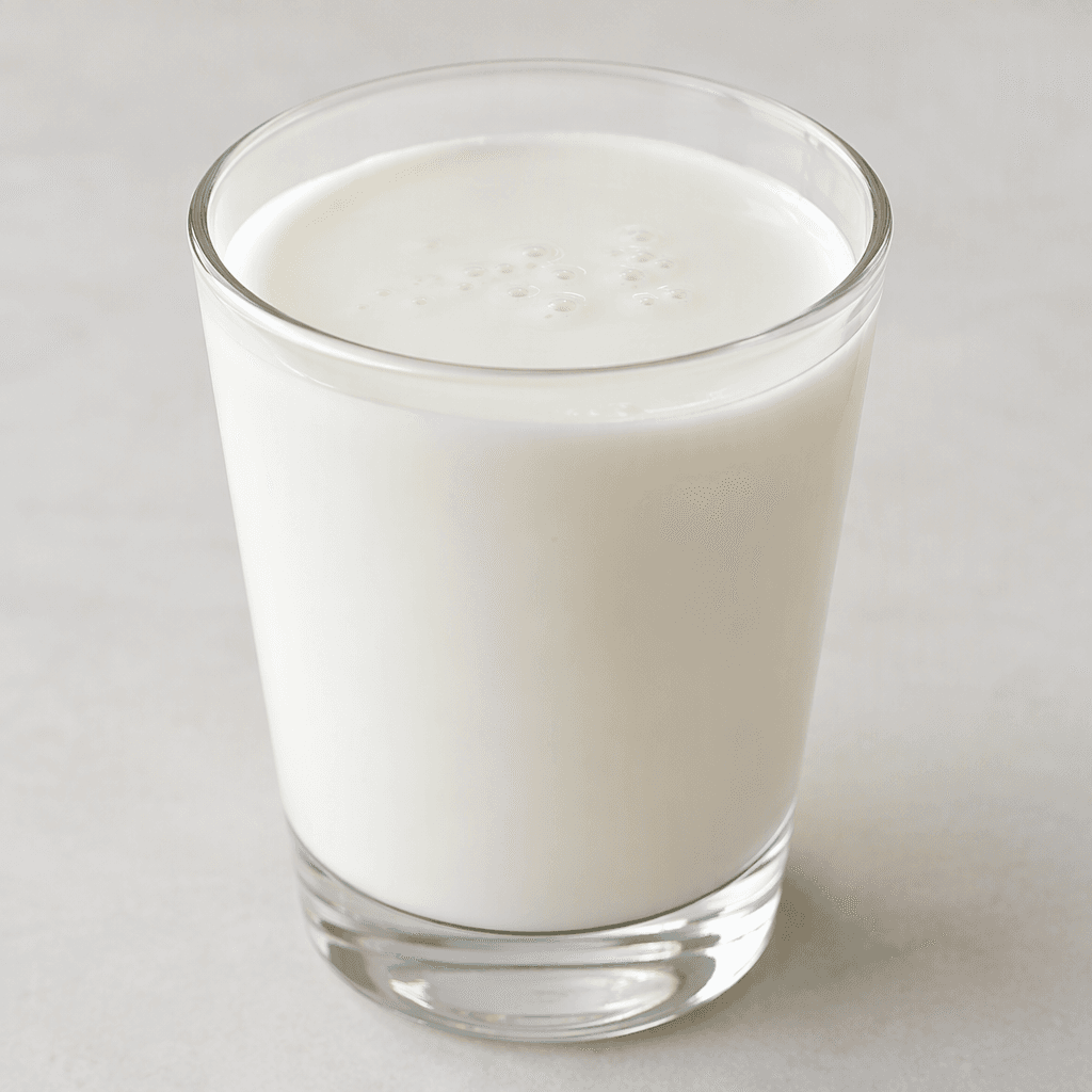 An opaque white, smooth and glossy cultured milk drink with a slightly thick, pourable texture, served in a clear glass with a few tiny bubbles on the surface.