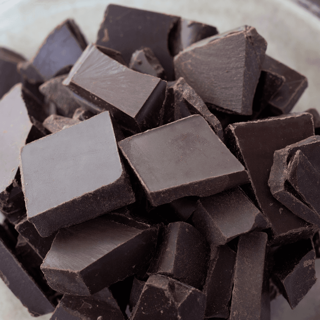 Dark, nearly black-brown chocolate sits in thick, roughly rectangular pieces, with a smooth sheen and a firm, slightly uneven surface.
