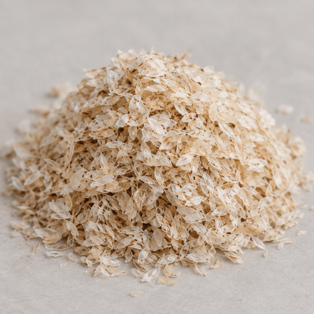 A small mound of pale beige psyllium husks, made up of thin, translucent, papery flakes with a light, airy texture.