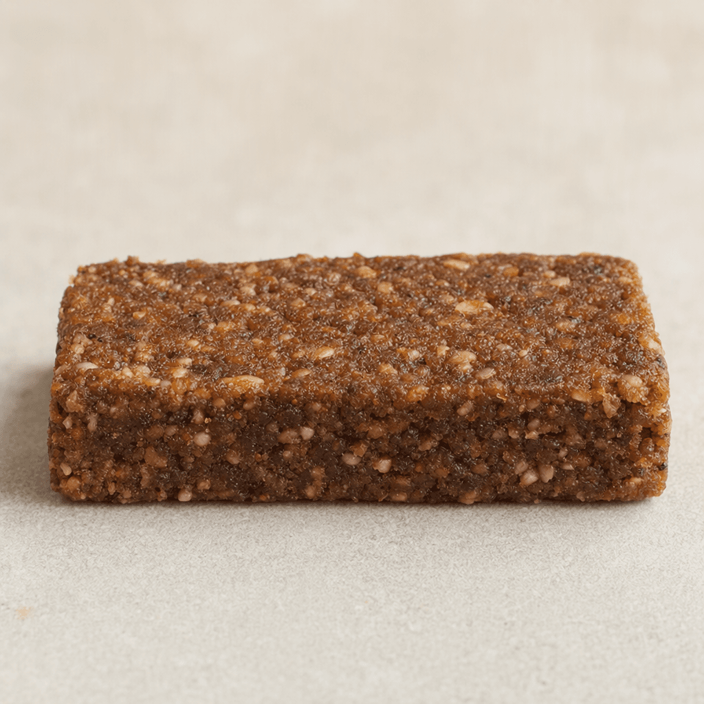 A compact, oblong rectangular fiber bar with a dense, slightly rough brown surface, uneven edges, and small lighter flecks visible throughout.