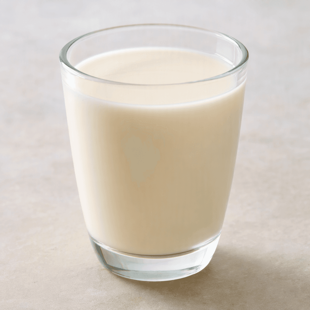 A glass of smooth, opaque almond milk, pale ivory with a faint beige tint and a level, unadorned surface.