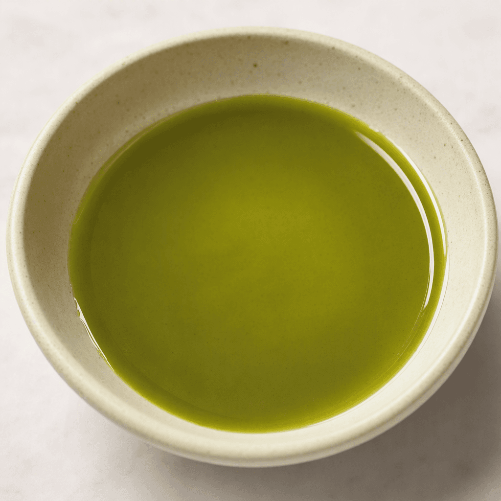 A glossy, translucent green oil with a smooth surface, pooled in a small dish.