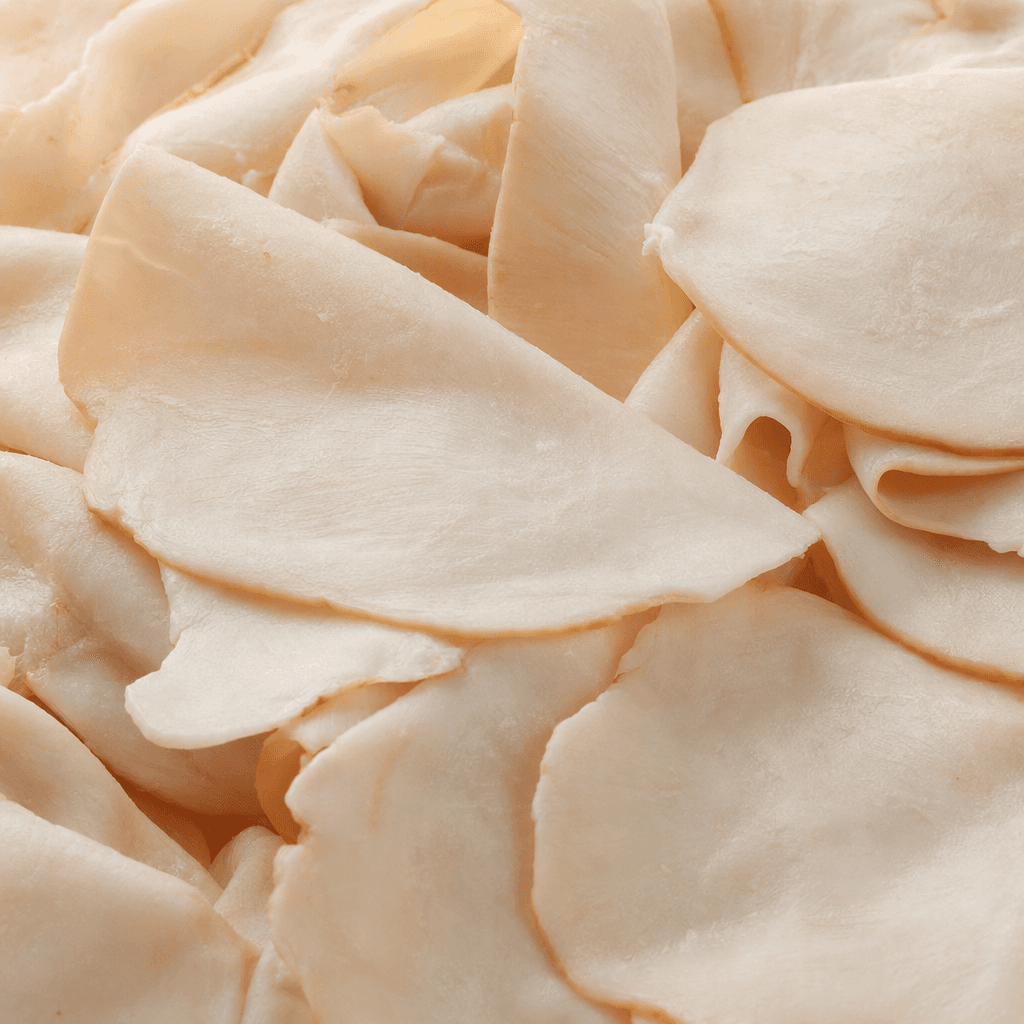 Thin, overlapping slices of processed chicken breast are pale pink-beige, with a smooth, slightly moist surface and softly rounded, irregular edges.