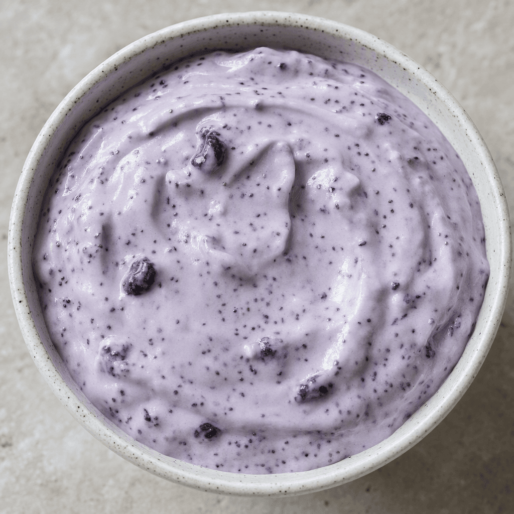 Thick, creamy pale-purple yogurt is served in a small bowl, speckled with tiny black chia seeds and dotted with dark blue-purple blueberry pieces.