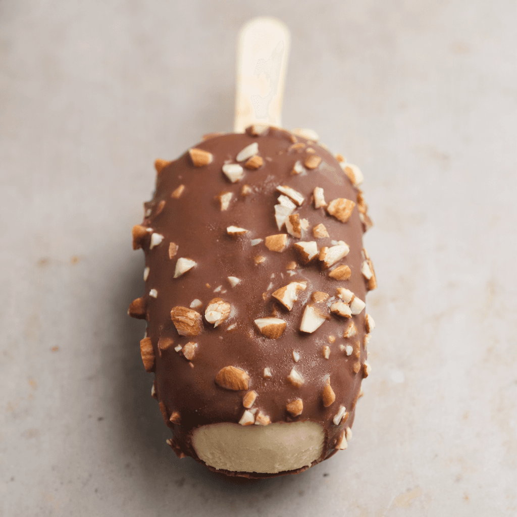 Small, bite-sized oval ice cream bars are coated in a thin brown chocolate shell studded with chopped almond pieces, with pale cream-colored ice cream visible at the ends and each bar on a short stick.