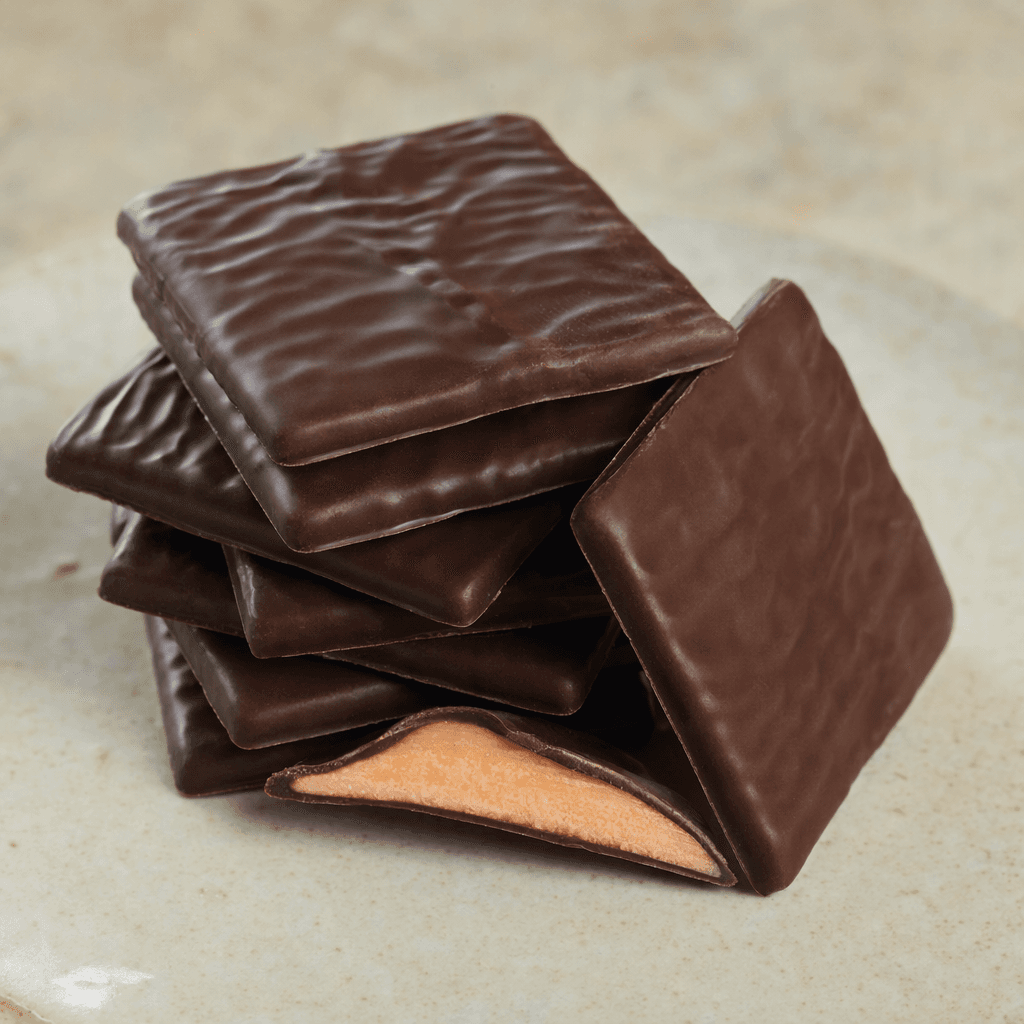 Thin, flat rectangles of dark brown chocolate with smooth, slightly glossy surfaces, arranged in an overlapping stack beside a broken piece showing a pale orange filling.