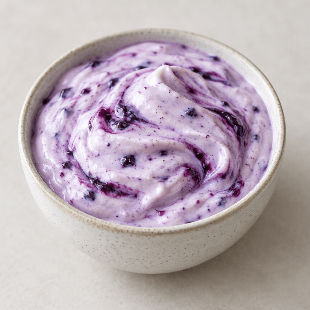 Thick, smooth pale lavender yogurt with darker purple blueberry swirls and tiny deep-blue fruit flecks, served in a small bowl.