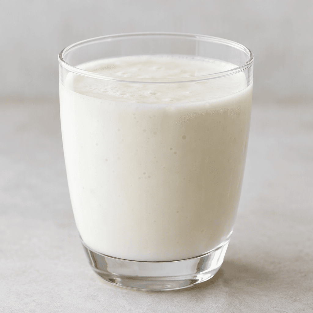 A pale white, smooth and slightly thick fermented milk drink poured into a clear glass.