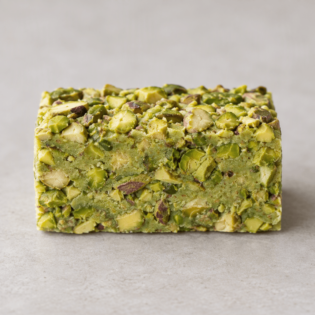 A compact rectangular bar with a firm, pale green interior densely packed with chopped pistachios, their varied green tones and beige shells visible across the cut surface and top.