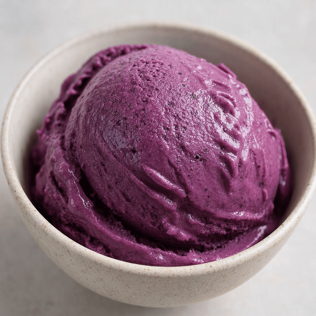 A scoop of deep purple aronia ice cream with a smooth, creamy texture, served in a small bowl.