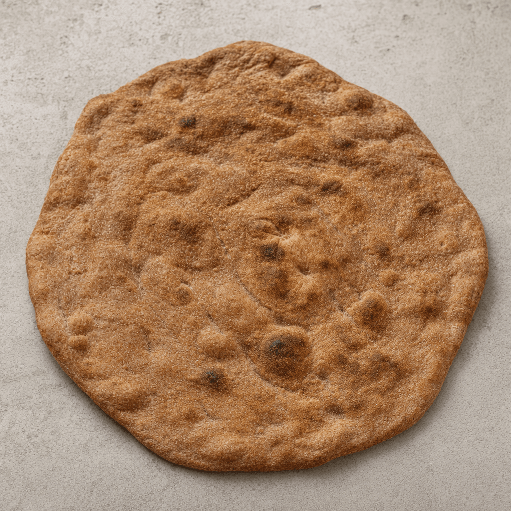 A thin, broad, roughly oval rye flatbread with a matte brown surface, darker toasted patches, and a few small bubbles and creases.