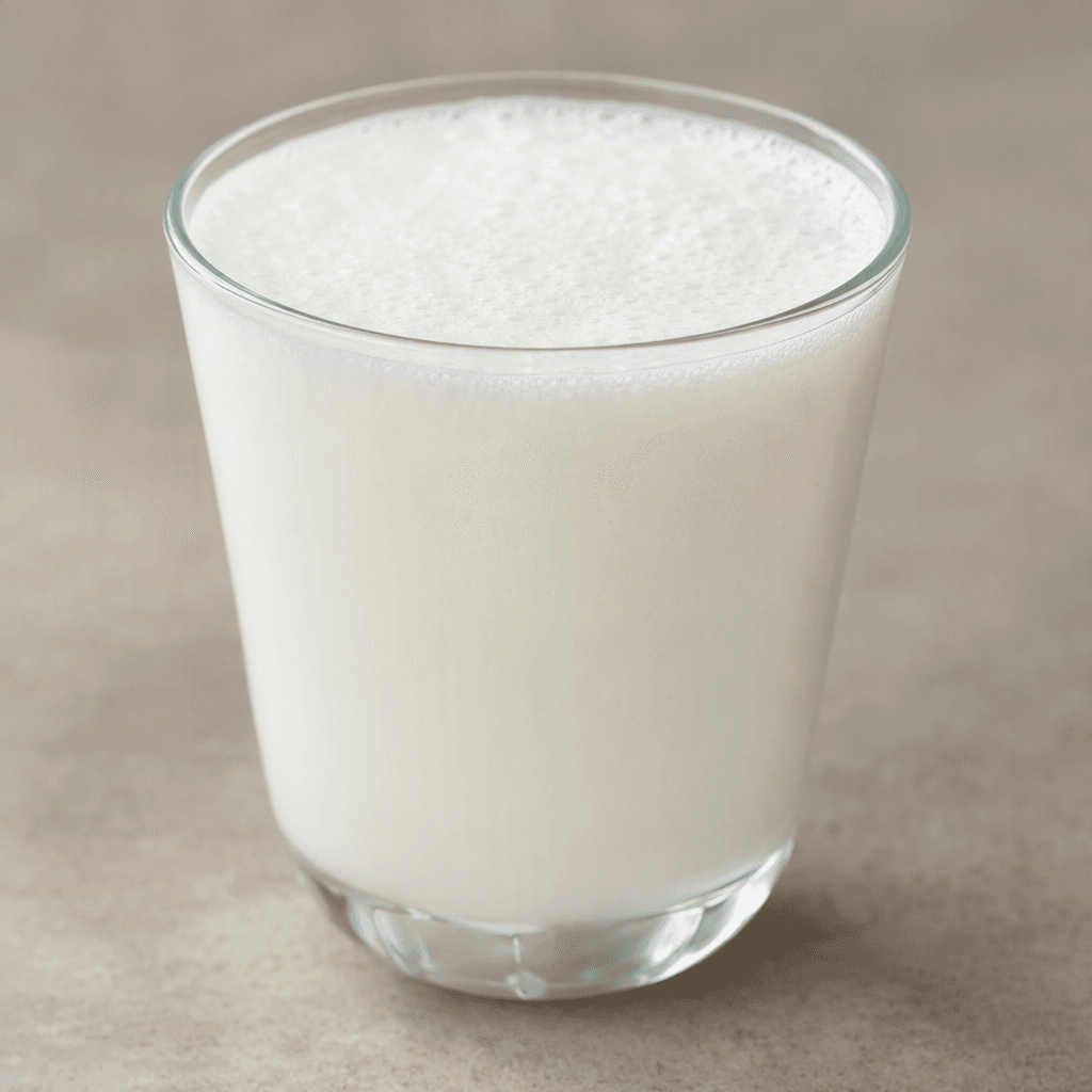 An opaque milky-white, pourable yogurt drink with a smooth texture and a thin layer of fine foam on top, served in a clear glass.