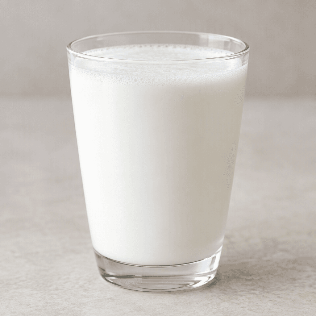 An opaque white, smooth and fluid drink with a thin layer of fine foam on top, served in a clear glass.