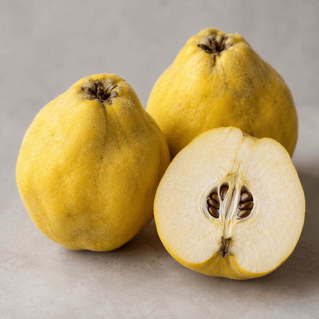 Whole quinces with round, slightly irregular pear-like shapes, golden-yellow skin covered in a fine velvety fuzz, alongside a cut quince showing firm pale cream flesh and a small central seed cavity.