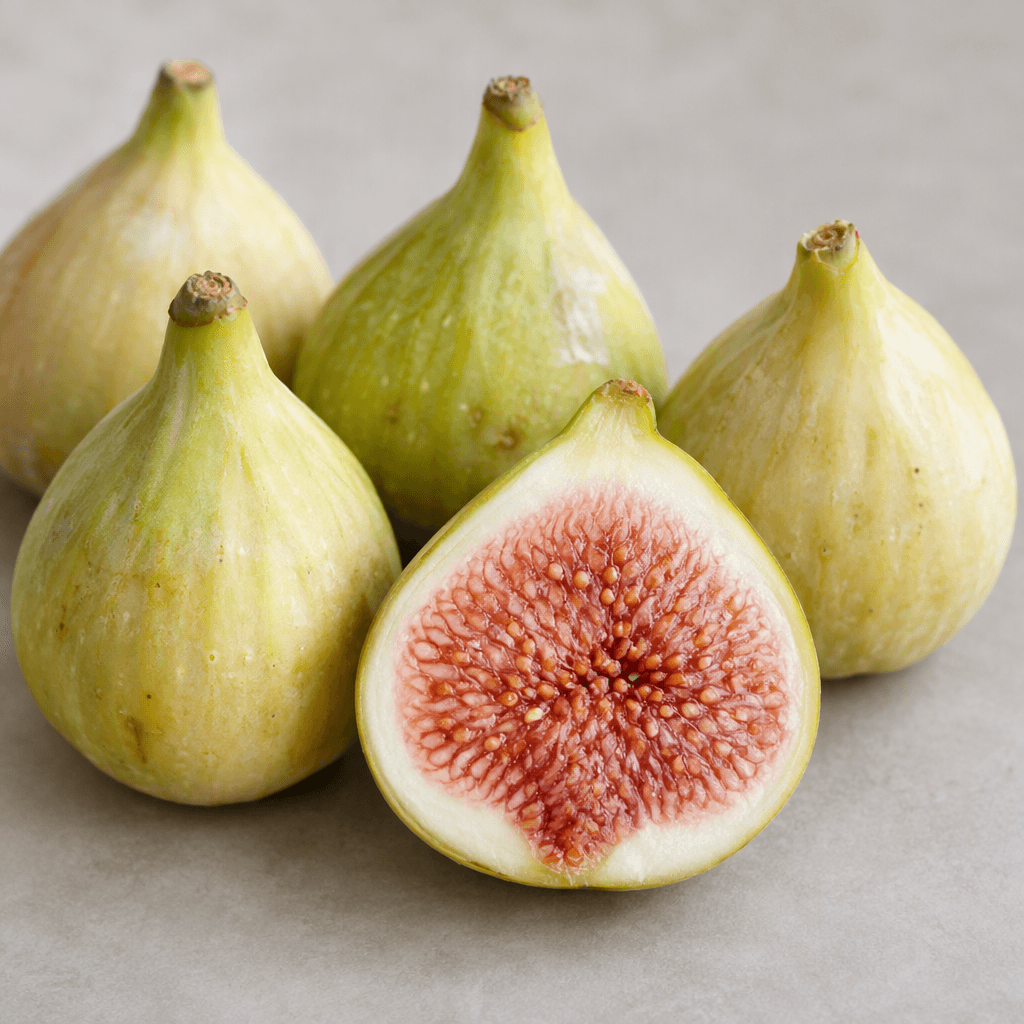 Several small, pear-shaped white figs with pale green to creamy yellow skin are arranged with one cut open, revealing soft pink flesh densely speckled with tiny pale seeds.