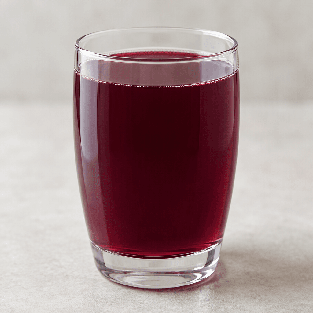 A deep burgundy-purple, slightly translucent fruit drink sits in a clear glass, with an even colour and no visible pieces of fruit.