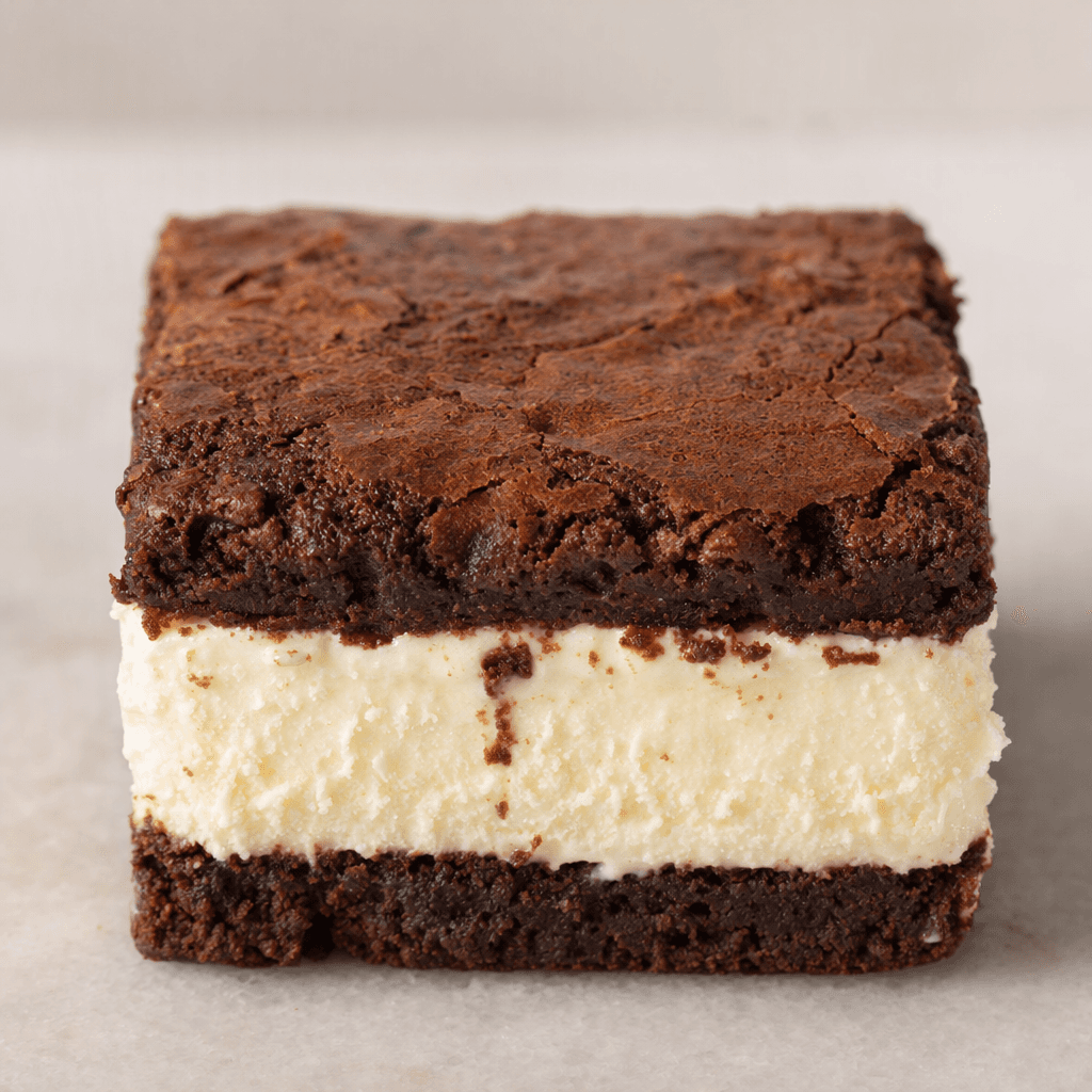A small rectangular dessert with two dark chocolate-brown, slightly uneven brownie layers enclosing a thick pale cream-colored ice-cream layer, with a few crumbs along the edges.