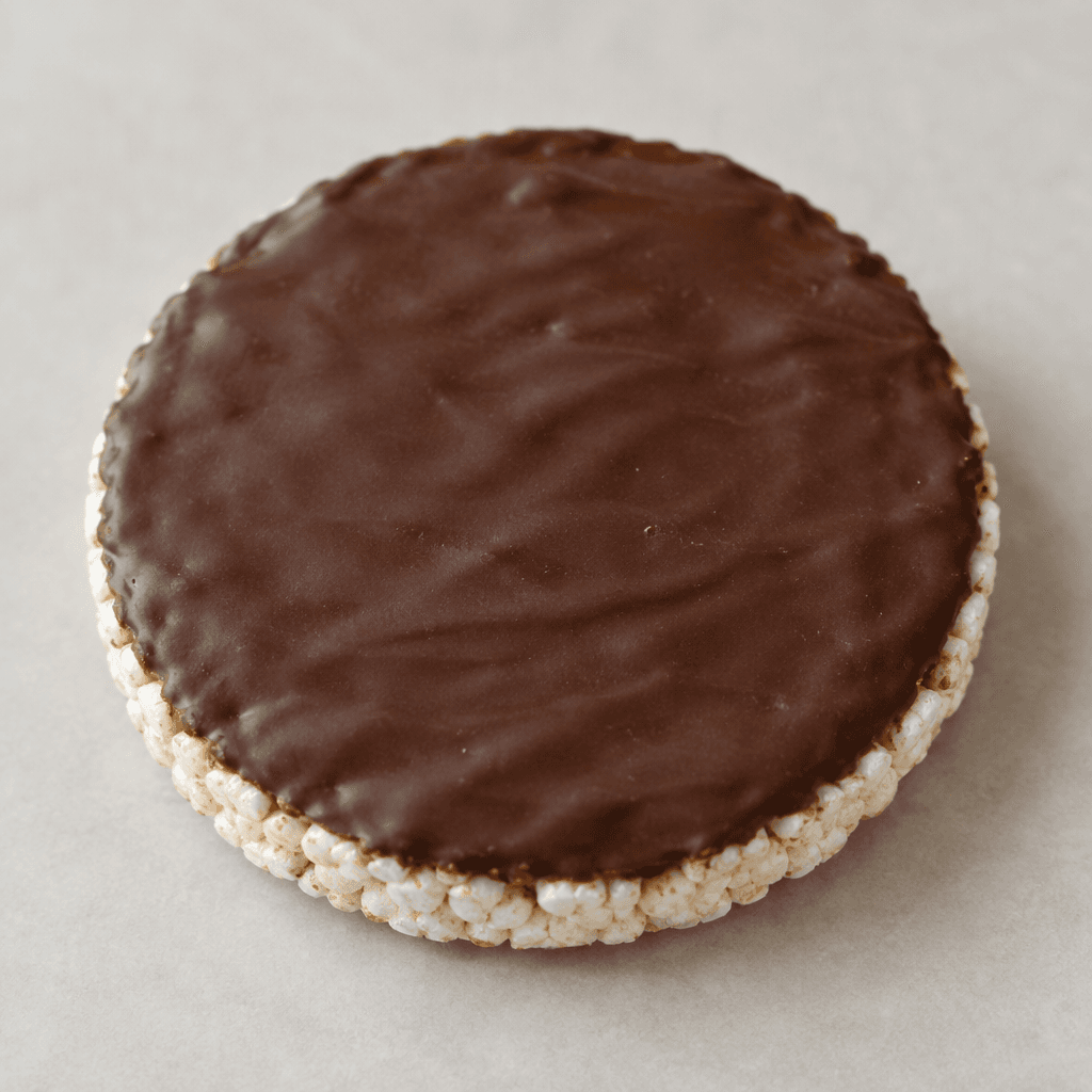 A round, flat, lightly puffed rice cake with a smooth dark-brown chocolate coating on one side and a pale off-white rice edge visible around it.