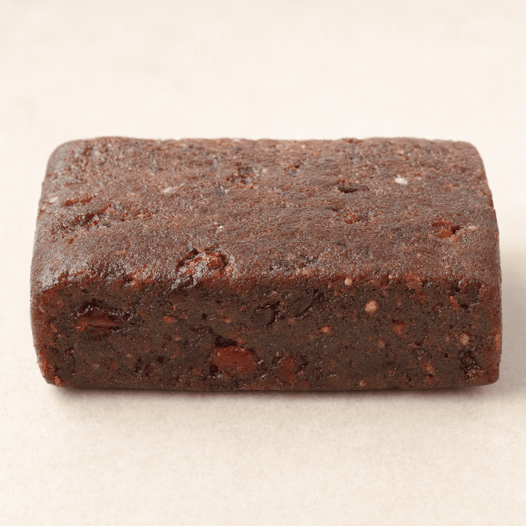 A compact rectangular cocoa-brown bar with a dense, slightly rough surface and small red fruit pieces visible throughout.