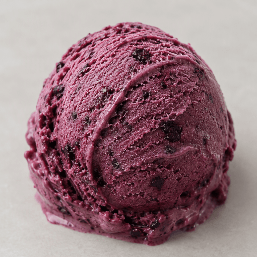 A scoop of creamy ice cream in deep mulberry-purple, with darker berry flecks and a softly ridged, slightly melting surface.