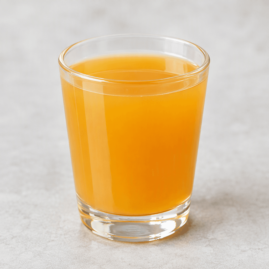 A translucent orange-golden fruit drink with a smooth, pulp-free appearance, shown as a small serving in a clear glass.
