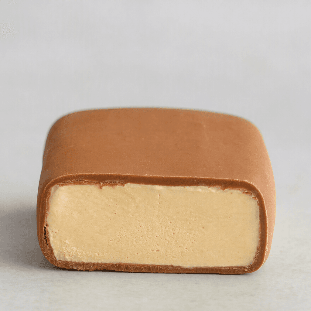 A small, rectangular ice-cream bar with rounded edges, covered in a smooth light-brown chocolate coating and showing a pale caramel-coloured ice-cream centre where cut.
