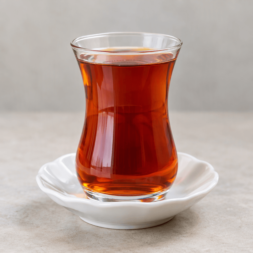 A clear tulip-shaped glass holds translucent reddish-amber tea with a faint sheen and no visible garnish, resting on a small saucer.