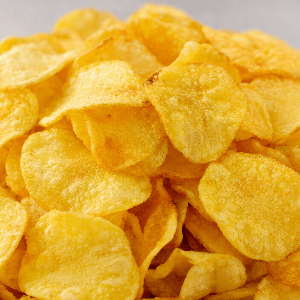 Small, thin, golden-yellow potato crisps with uneven edges and a lightly bubbled, crisp-looking surface are piled together.