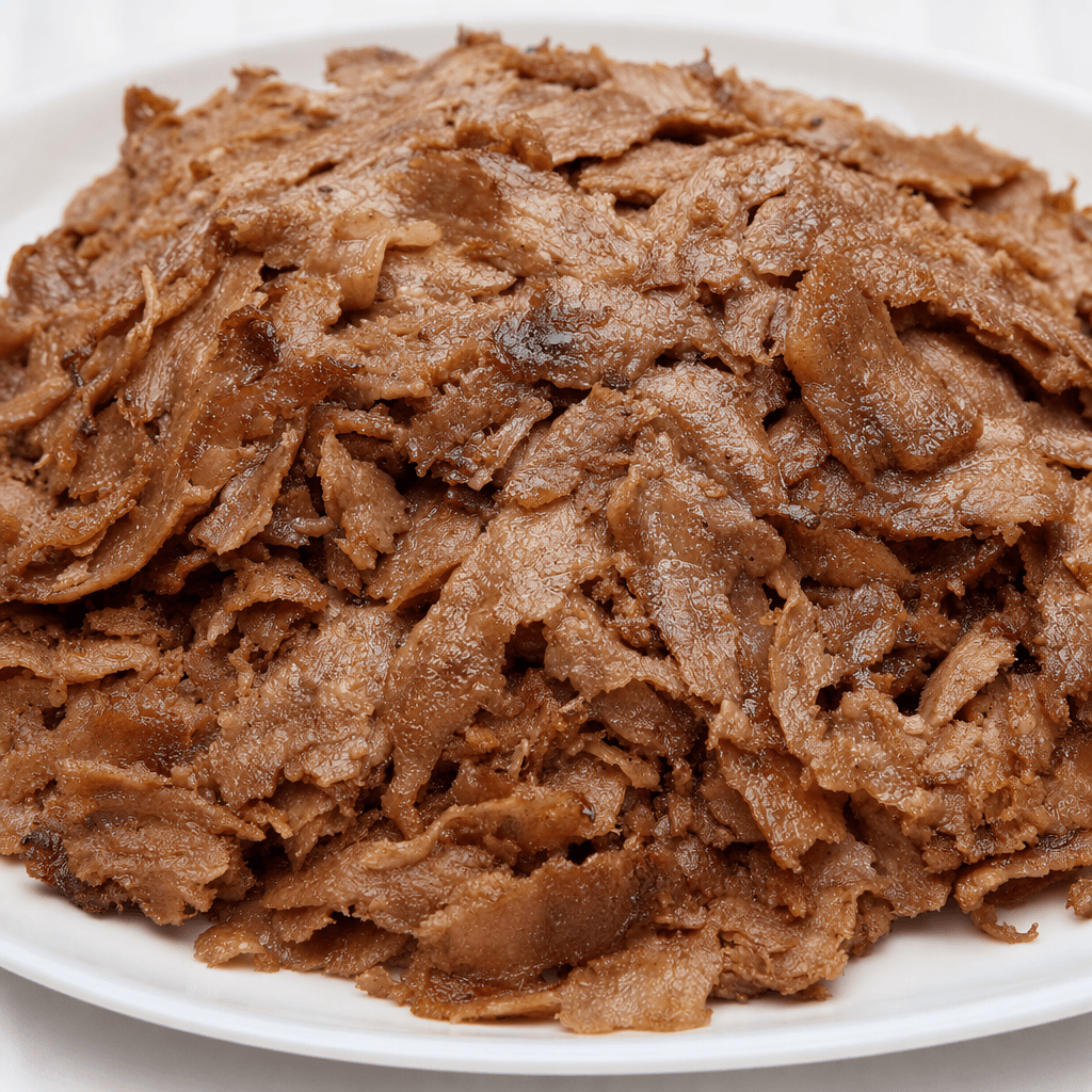 Thin, irregular slices of beef with browned edges and a moist, fibrous interior are piled on a plain plate.