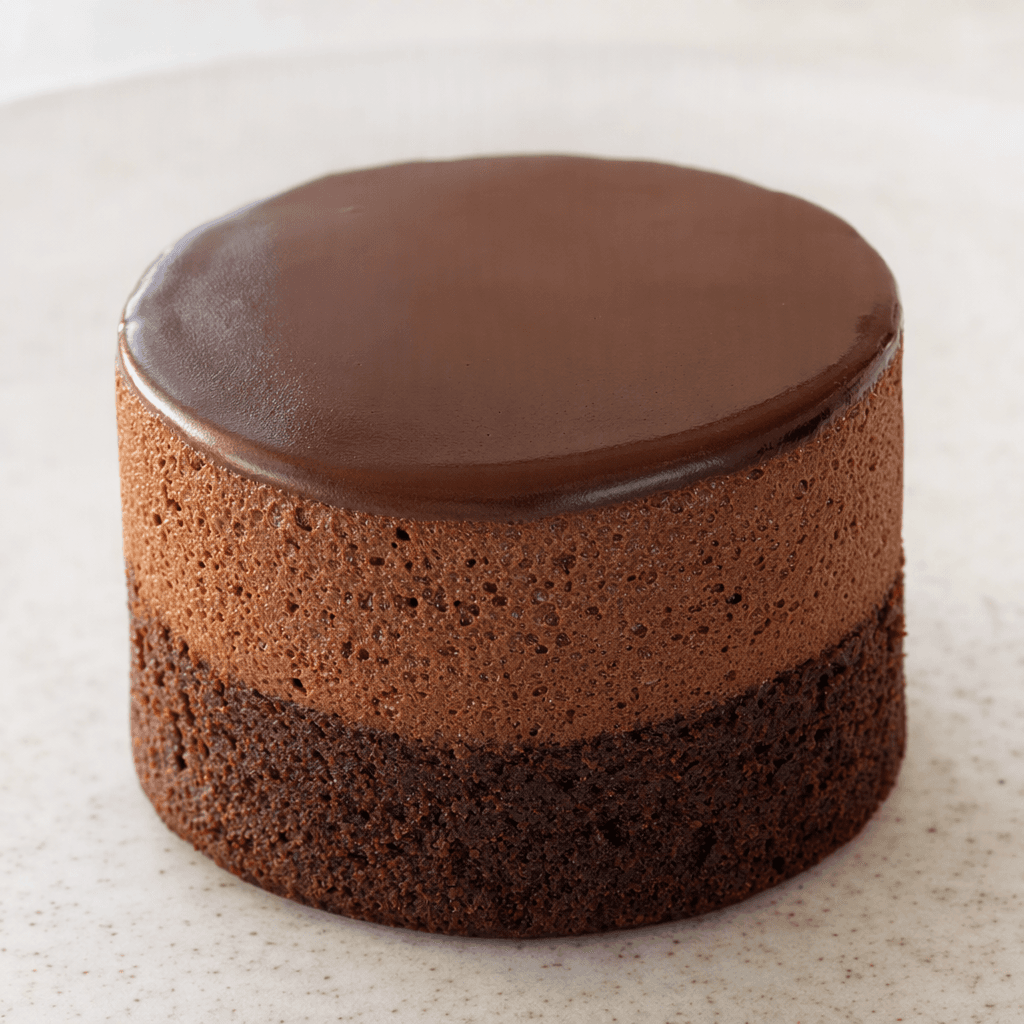 A small, dark-brown chocolate cake with a soft, airy mousse layer and a smooth chocolate-coated surface.