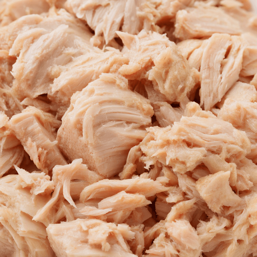 Moist, pale pinkish-beige pieces of tuna, loosely broken into uneven chunks and flakes with a soft, fibrous texture.