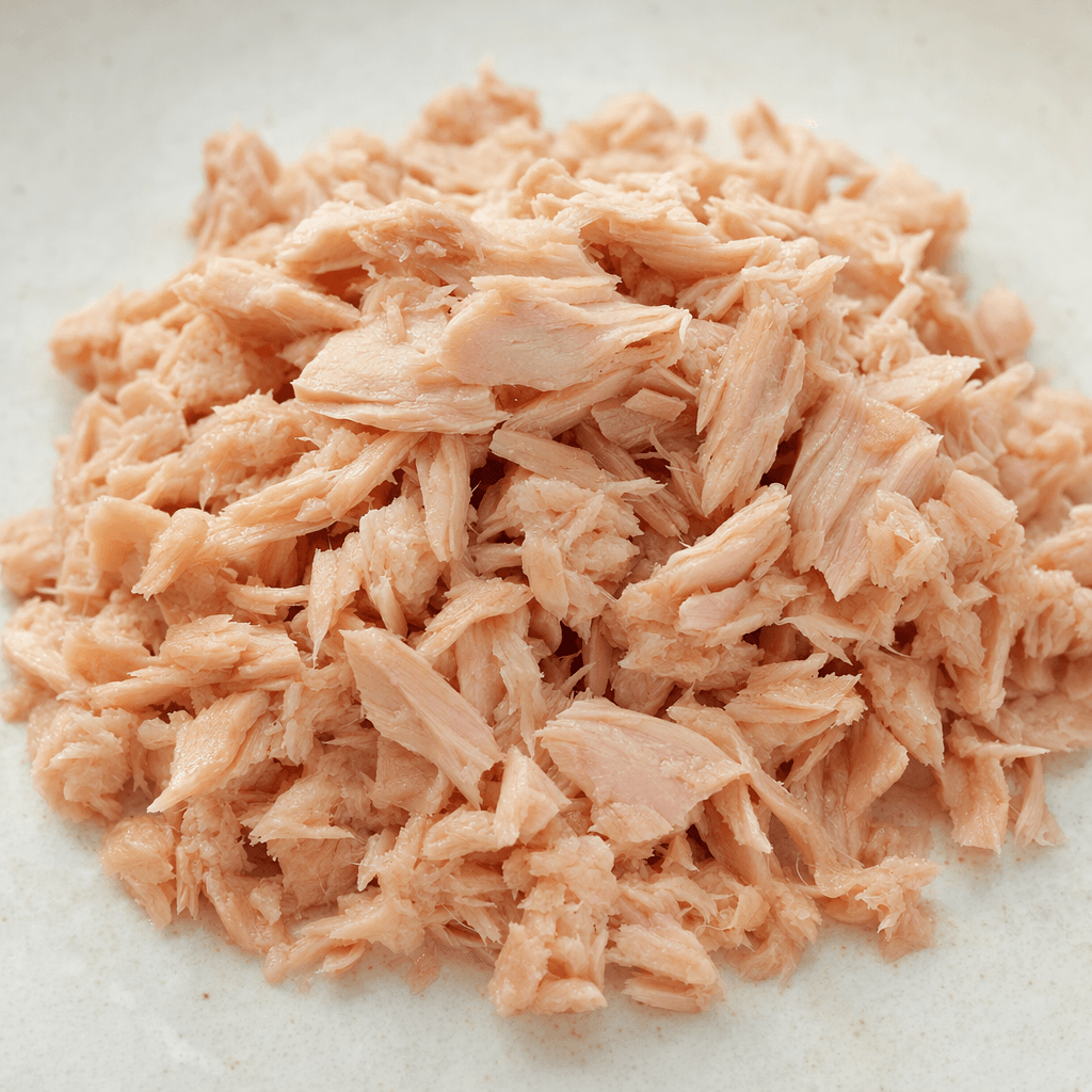 A small mound of drained tuna sits in loose, moist flakes and chunks, ranging from pale pink to light beige.