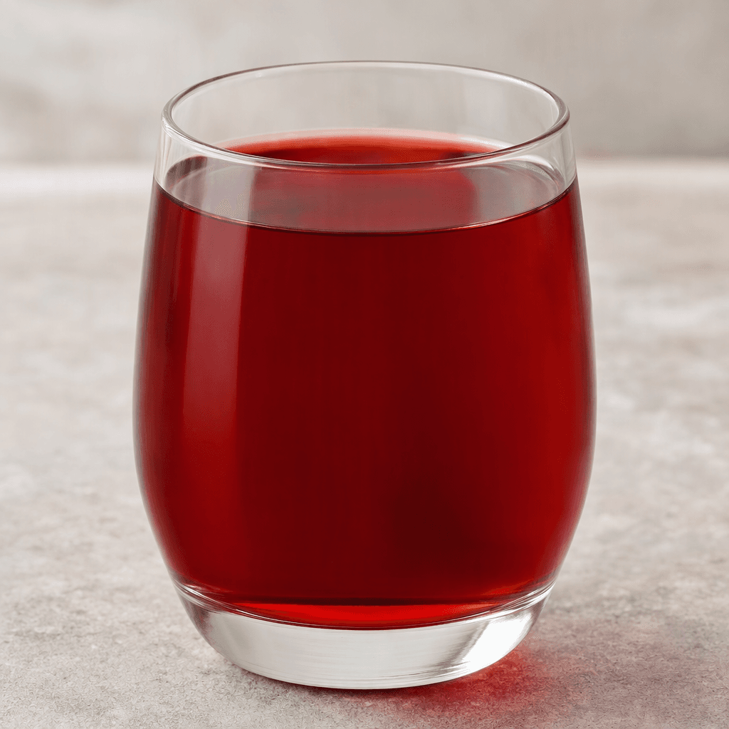 A clear, deep ruby-red drink with a slight garnet tint, served in a transparent glass, its surface catching soft highlights and showing no visible pieces.