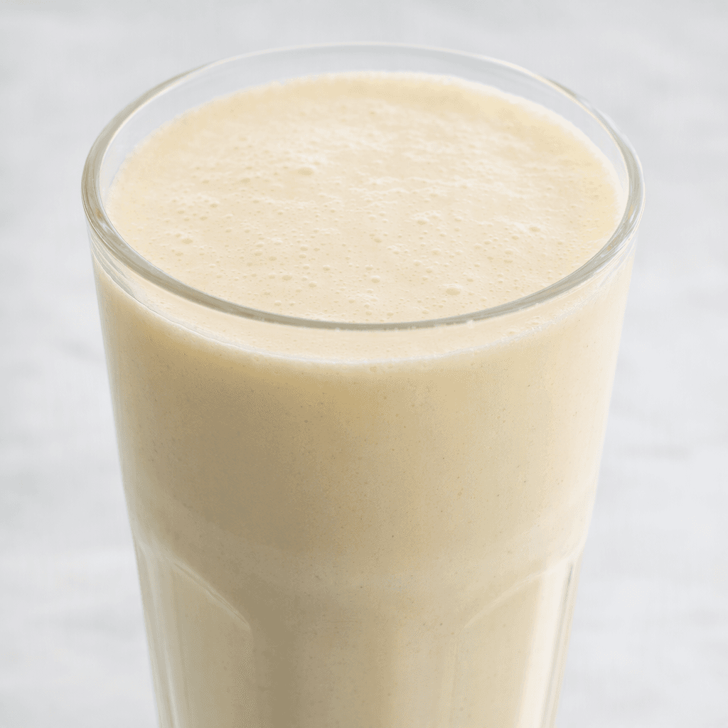 A thick, smooth, pale cream-colored vanilla milkshake with a lightly frothy surface.
