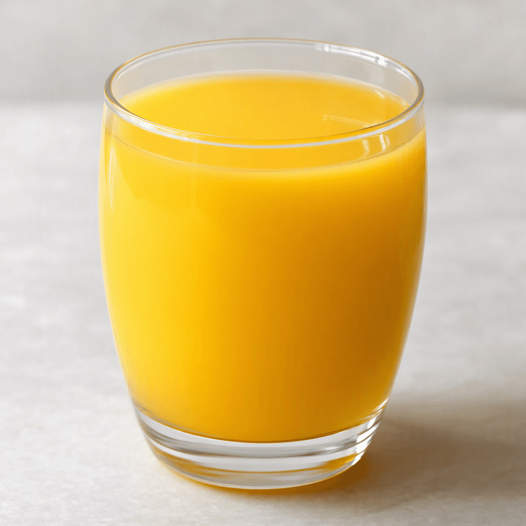 A smooth, opaque golden-orange fruit juice fills a clear glass, with an even colour and no visible pulp or garnish.