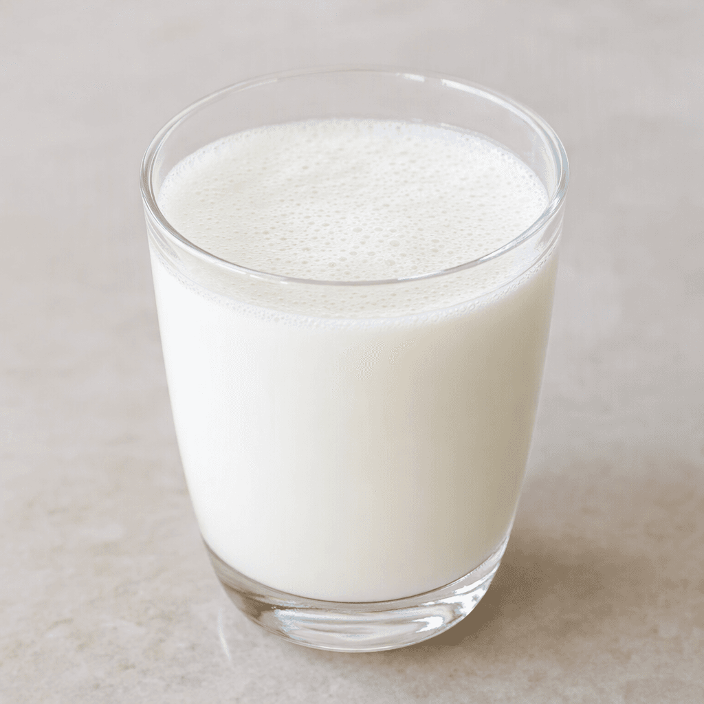 An opaque white, smooth yogurt drink with a light layer of fine foam, served in a clear glass.